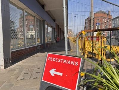 A pedestrians sign pointing along the path next to fencing outside the former Hardshaw Centre